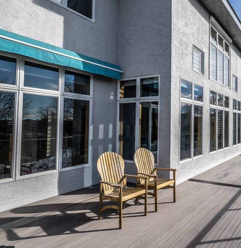 Composite deck with Adirondack chairs along tall stucco walls and floor-to-ceiling windows