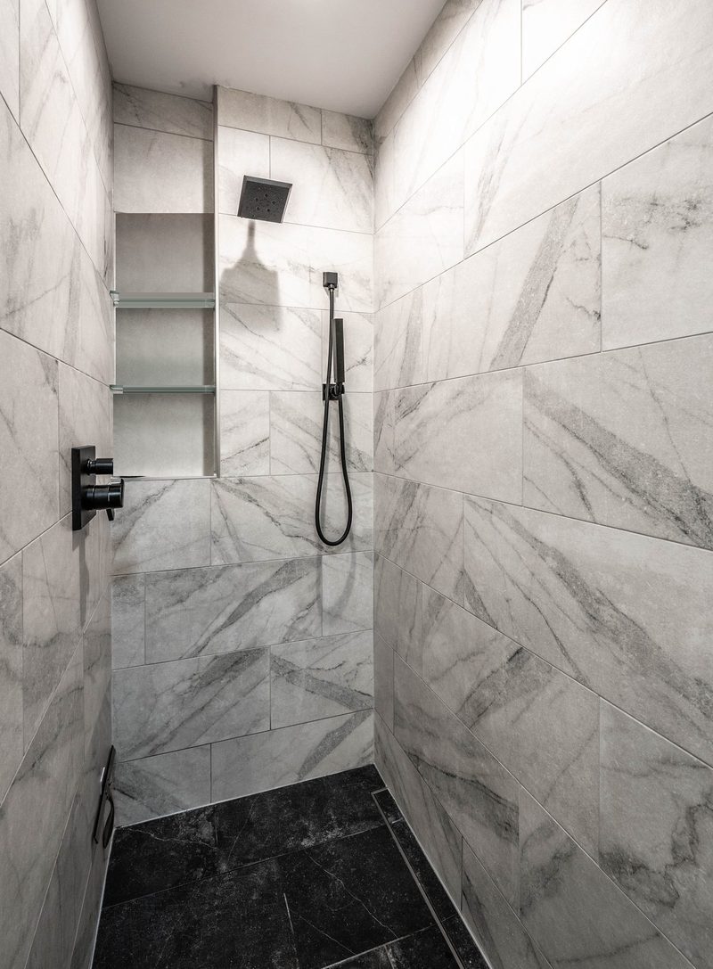 Walk-in shower with large-format marble-look tile, black fixtures and a dark tile floor