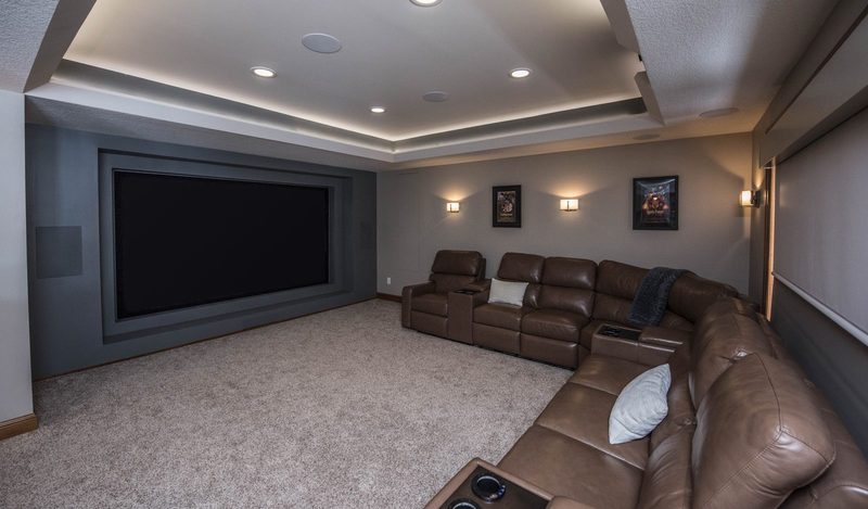 Basement home theater with a large screen, tray ceiling with cove lighting and a leather sectional
