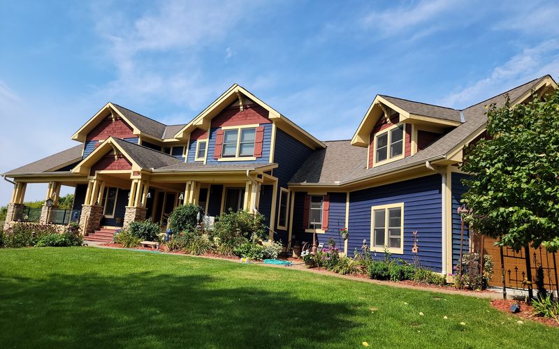 Craftsman home with navy lap siding, red board-and-batten gables, cream trim and stone-based porch columns