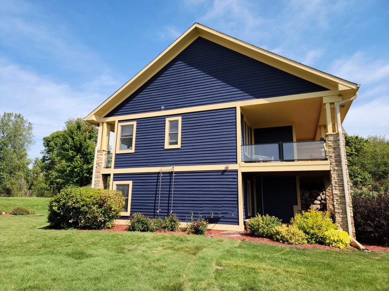 Two-story home with navy lap siding, cream trim, stone columns and a covered lower patio