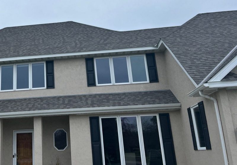 New charcoal architectural shingle roof with white fascia and gutters on a two-story stucco home