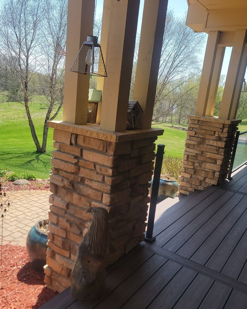 Covered porch with stacked-stone column bases, wood posts and composite decking overlooking a lawn